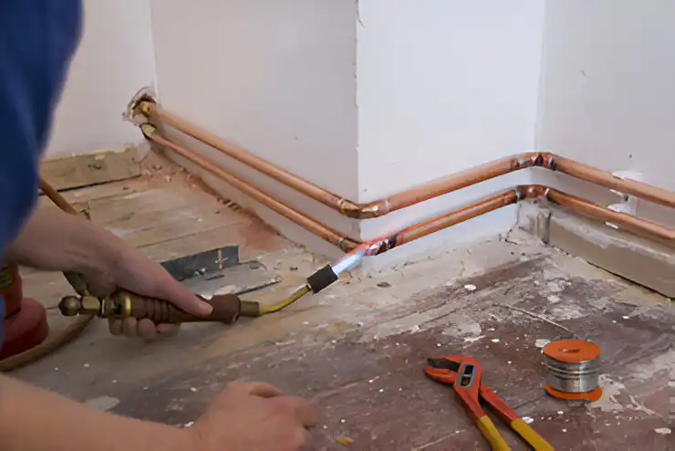 A man is installing copper pipes in a room.