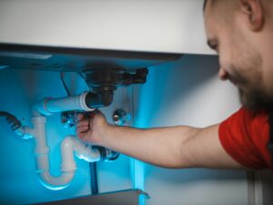 A man is engaged in plumbing work, fixing a pipe located under a kitchen sink.