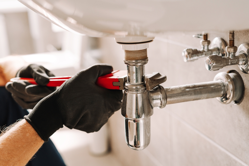 Plumber in black gloves fixes a sink pipe with a wrench in a bathroom